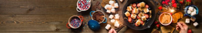 Bowls of marshmellows, graham crackers, chocolate, sprinkles, strawberries, and blueberries on a table