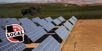a field of solar panels next to a vineyard with a support local California logo