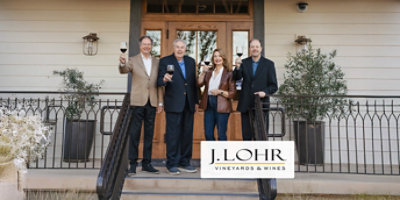 3 men and 1 woman holding filled wine glass on a porch with J. Lohr Vineyards and Wines logo