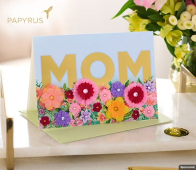A Mother's Day card sitting on a desk next to a vase of flowers.