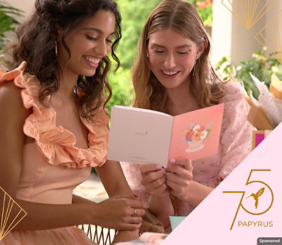 Two women sitting next to each other, reading a greeting card and smiling.