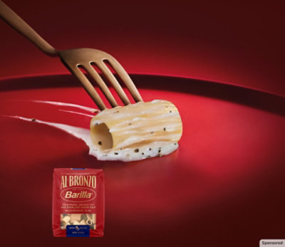 Barilla® Al Bronzo® pasta on a fork with a box of pasta in front of the fork.