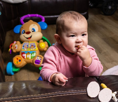 Baby is eating finger food some toys were there around her