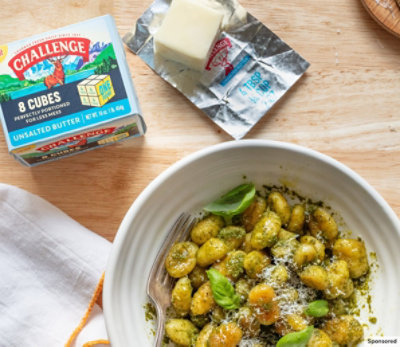 Bowl of pesto gnocchi on a wooden table with Challenge Butter Cubes. 