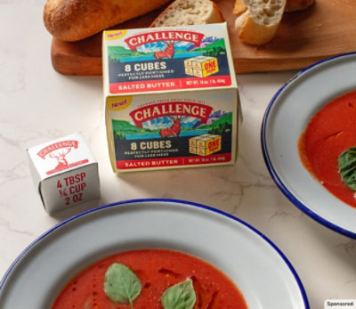 Bowls of tomato soup with Challenge butter cubes on a marble countertop. 