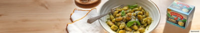 Bowl of pesto gnocchi on a wooden table with Challenge Butter Cubes. 
