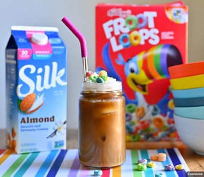Froot Loops iced latte with the cereal box and almond milk carton in the back. 