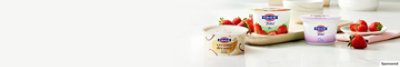 FAGE Creamy Dreamy cup and FAGE Total on glossy table top and strawberry on plate.