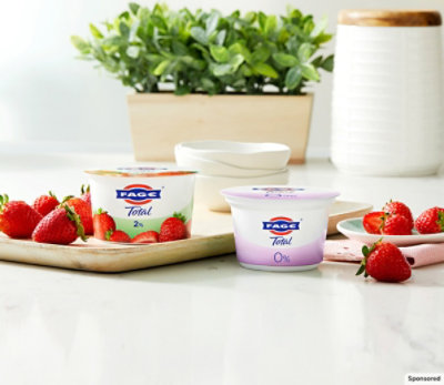 FAGE Creamy Dreamy cup and FAGE Total on glossy table top and strawberry on plate.