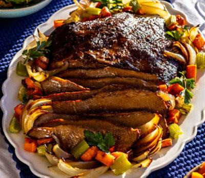 Sliced roast with roasted veggies on a ceramic serving platter.
