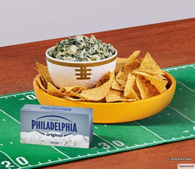 Creamy spinach artichoke dip, chips and Philadelphia cream cheese sit on a football-themed table. 