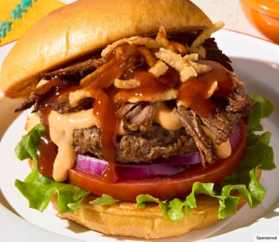 Close up of barbacoa burger with fried onions, tomato, onion and lettuce on a white plate.