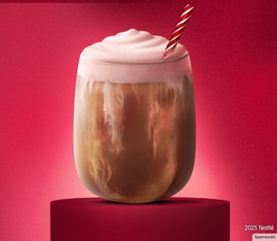 A cup of White Peppermint Mocha on a red background with a peppermint stick as a stirrer.