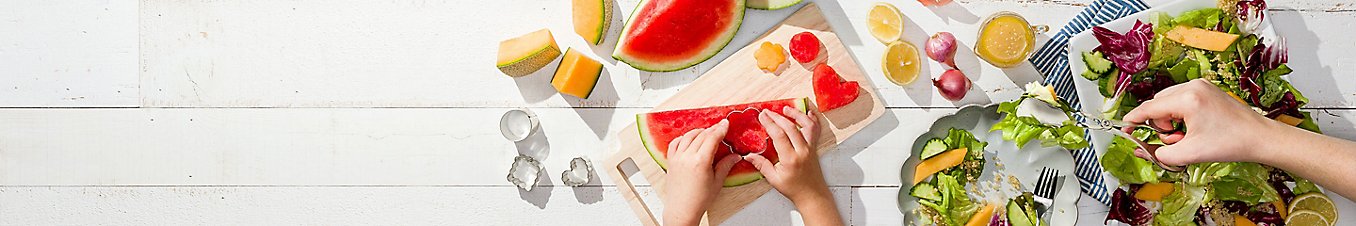 Cutting fruits with cookie cutters on a cutting board and preparing plates of salad