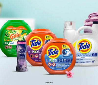 Tide, Gain, and Downy laundry care products on a counter with a laundry basket and pink flower.
