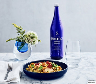 A bottle of Saratoga Water on a table with food.
