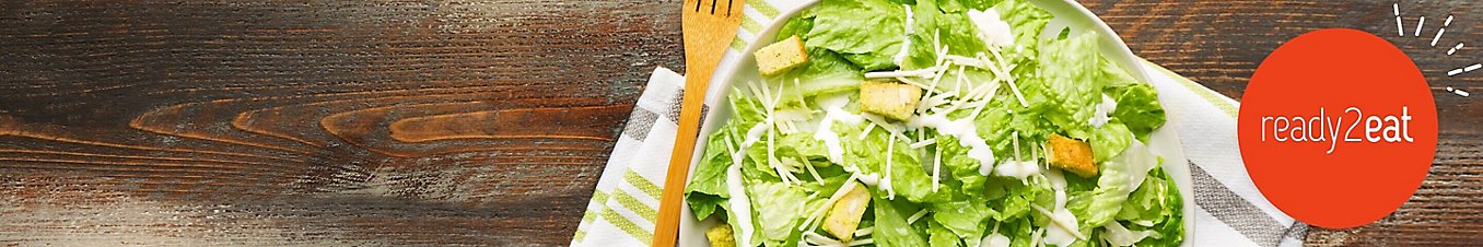 A bowl of Caesar salad next to a wooden fork