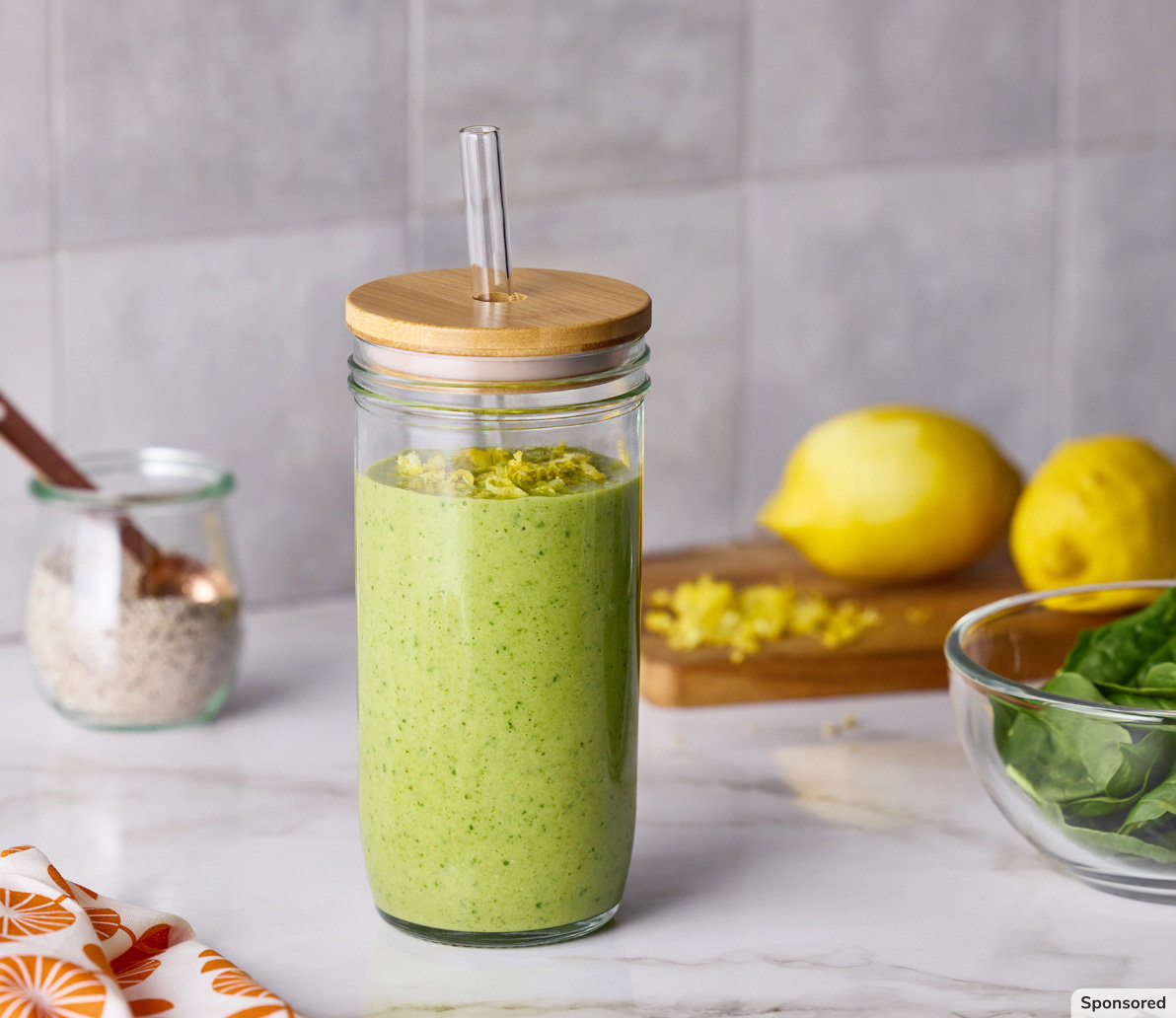 Ready-to-drink green smoothie with lemons and spinch in the background.