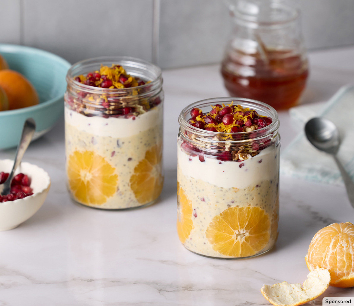 Two jars of overnight oats with honey and oranges in the background.