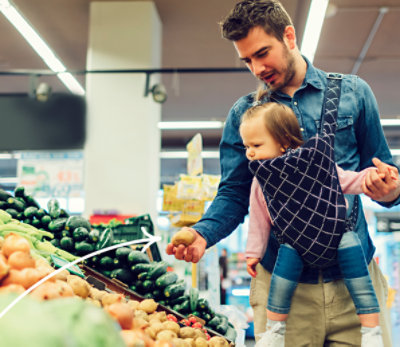 Man holding baby while shopping in produce department.