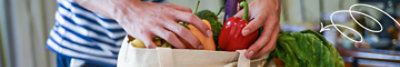 Someone putting fresh vegetables into a brown paper bag.