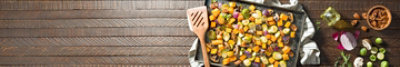 Roasted Veggies in tray on a table along with stirring wooden flat spoon and fresh nuts and vegetables 