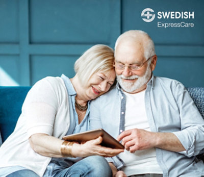 Happy couple looking at iPad on couch. Swedish ExpressCare.