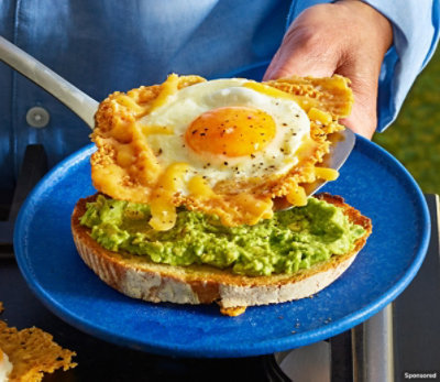 Man holding a crispy cheddar egg & avacado sandwich on a blue plate.