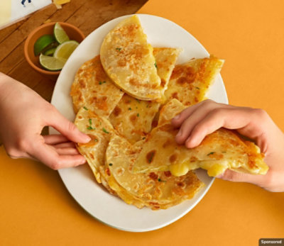 Children's hands taking a slice from a plate of melty quesadilla slices on a table.