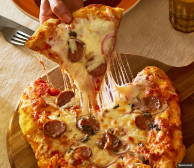 Slice of melty salami, red onion and oregano pizza being lifted out of pan.