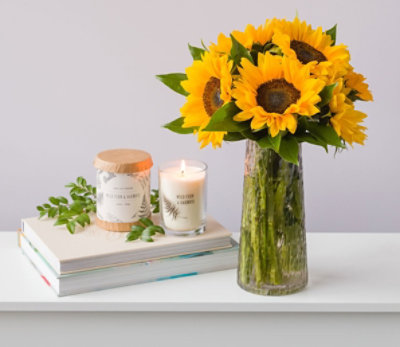 Sunflowers in a vase on a table next to candles and books